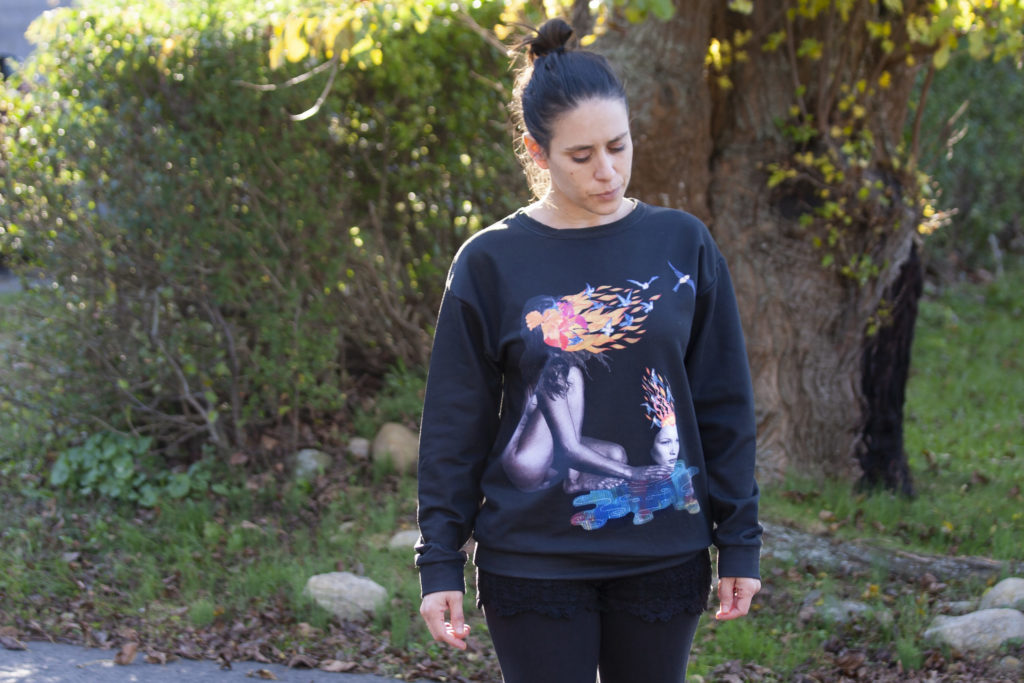 Yisca outdoors, wearing a sweatshirt printed with one of her collages