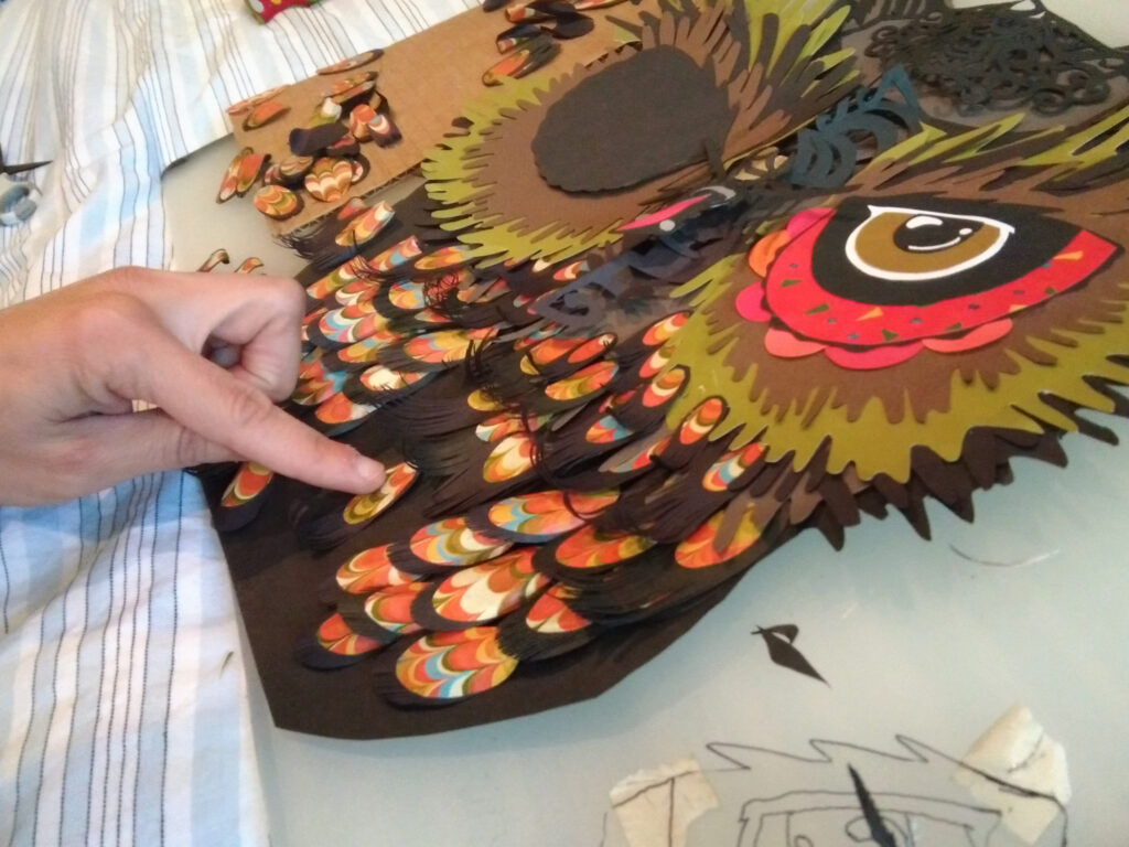 Placing small paper feathers on an owl collage